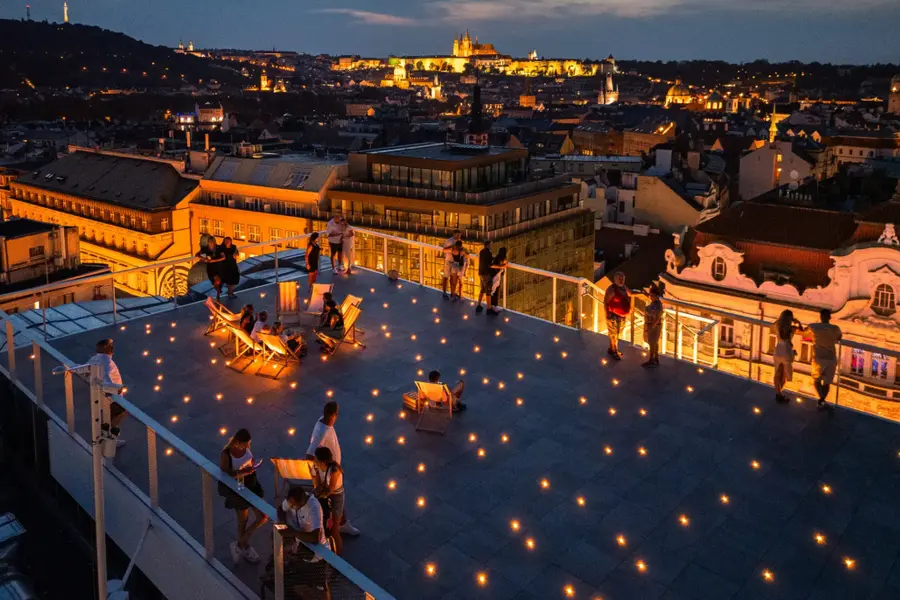 A rooftop terrace at nightfall, Prague Castle lit behind it.